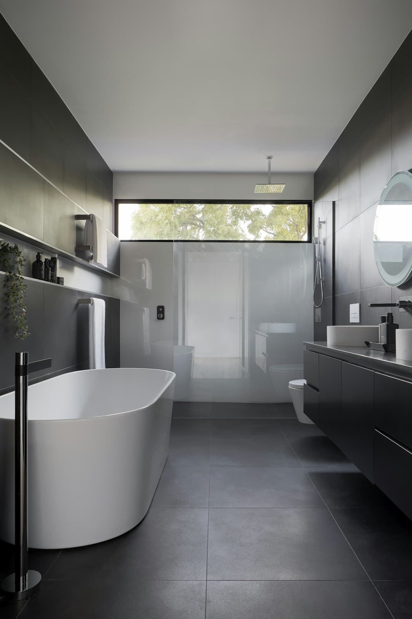 Quiet bathing space with charcoal surfaces, a freestanding bath, and soft natural light